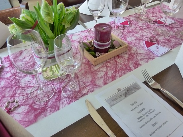 Spring table setting, green plants, purple lace runner, burgundy candle, wine glasses, menu at place setting 
